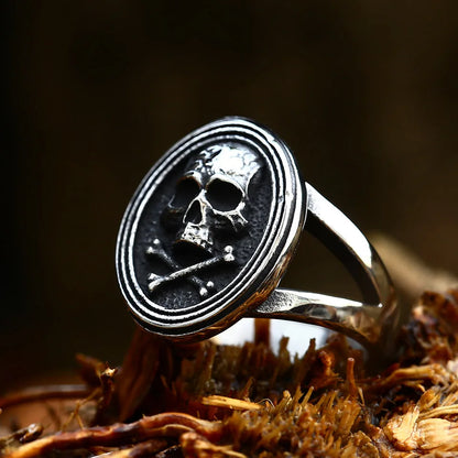 Side angle view of The Black Tide ring showing the oval design and skull detail set on textured wood.