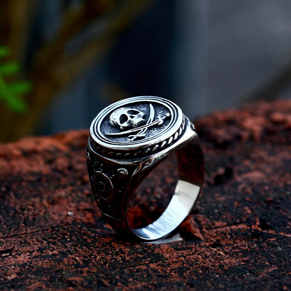 Full view of The Captain's Oath ring set on a rugged surface, showcasing the pirate-inspired design with a skull and ship's wheel.