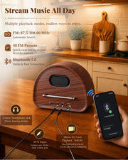 A wooden Bluetooth speaker shown on a kitchen counter with a hand holding a smartphone displaying a connected app, plus feature callouts and text about streaming music, FM range, presets, Bluetooth 5.0, headphone jack, AUX input, and micro SD card playback.