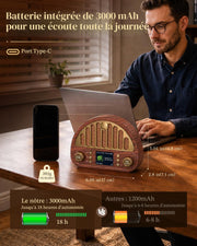 A man sits at a wooden table using a laptop next to a brown wood-grain portable radio with integrated speakers, a smartphone, and French text showing battery life and dimensions.